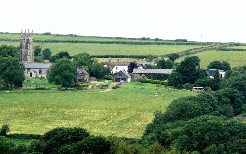 un grande campo verde con una casa e animali in essa di The Tack Room - a comfy cabin in North Devon a Bideford