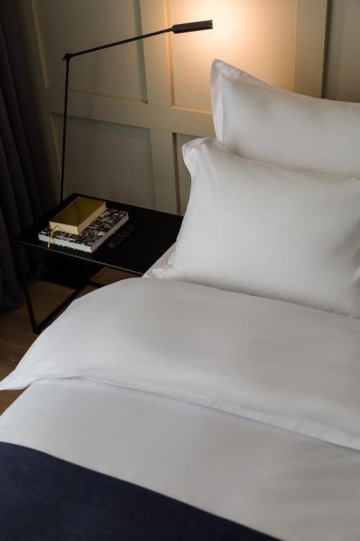 a bed with white sheets and pillows and a lamp at Bona Fide Main Square Designer Apartments in Zagreb