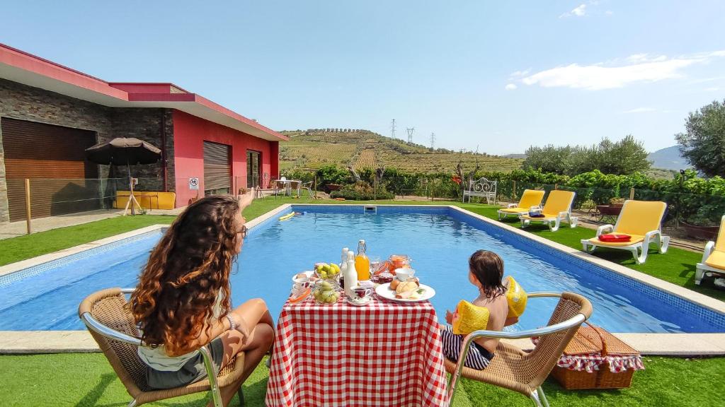 two women sitting at a table next to a pool at Quinta dos Padrinhos - Suites in the Heart of the Douro in Lamego