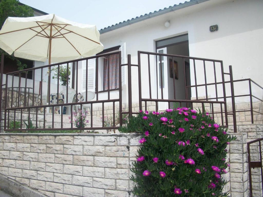 a house with a brick wall and an umbrella and flowers at Apartment Banjol 137 in Rab