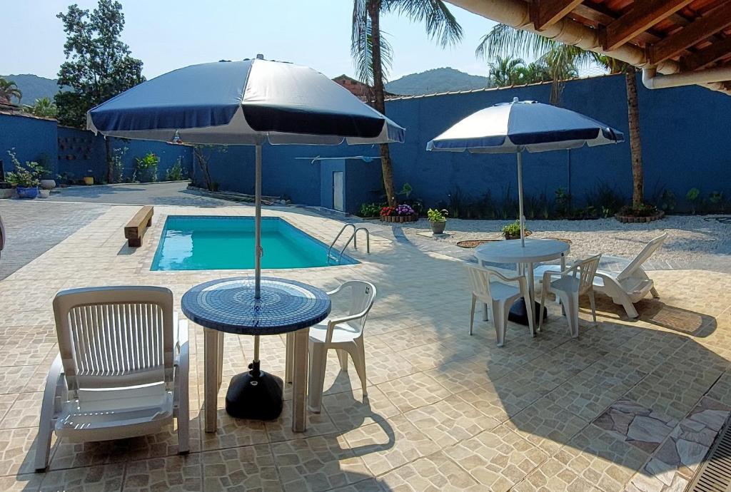 due tavoli e sedie con ombrelloni accanto a una piscina di Recanto Do Sossego Suítes Hospedagem Domiciliar na Praia a Boicucanga