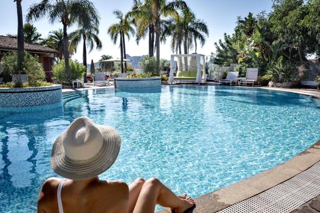 a woman in a hat sitting next to a swimming pool at Cruccùris Resort - Adults Only in Villasimius