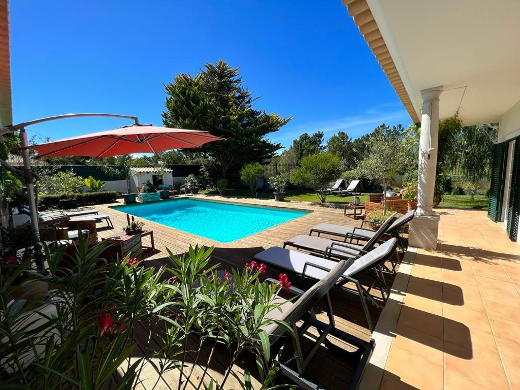 a swimming pool with lounge chairs and an umbrella at Buganvilias Do Meco Guest house in Sesimbra