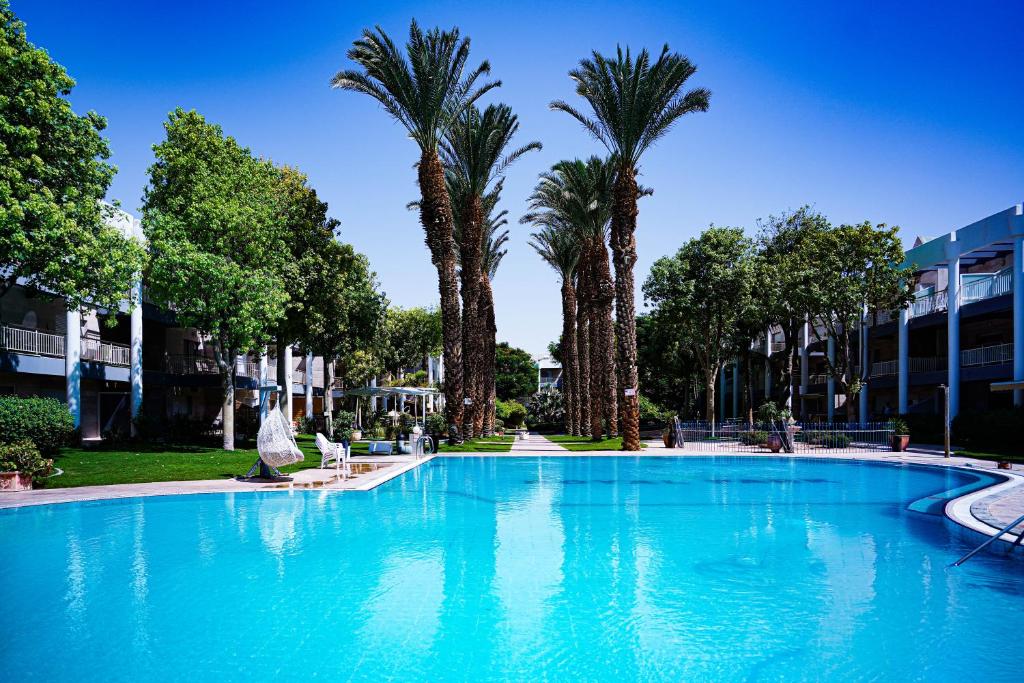 a large swimming pool with palm trees and a building at Royal Park By Sun and View in Eilat