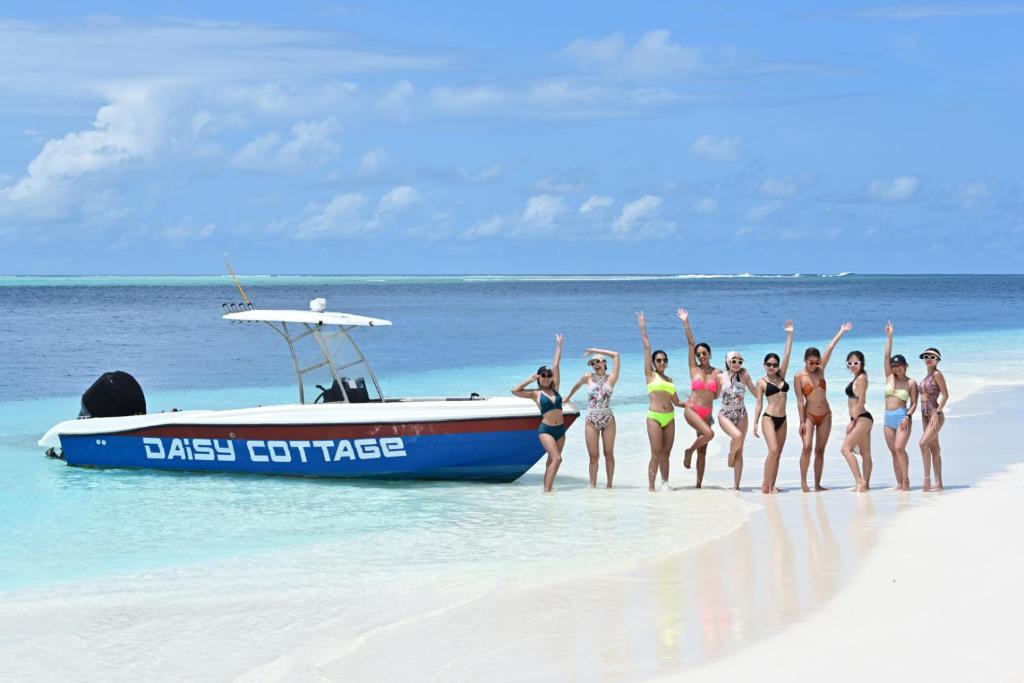 um grupo de mulheres em pé em uma praia ao lado de um barco em Daisy Cottage Dhangethi em Dhangethi