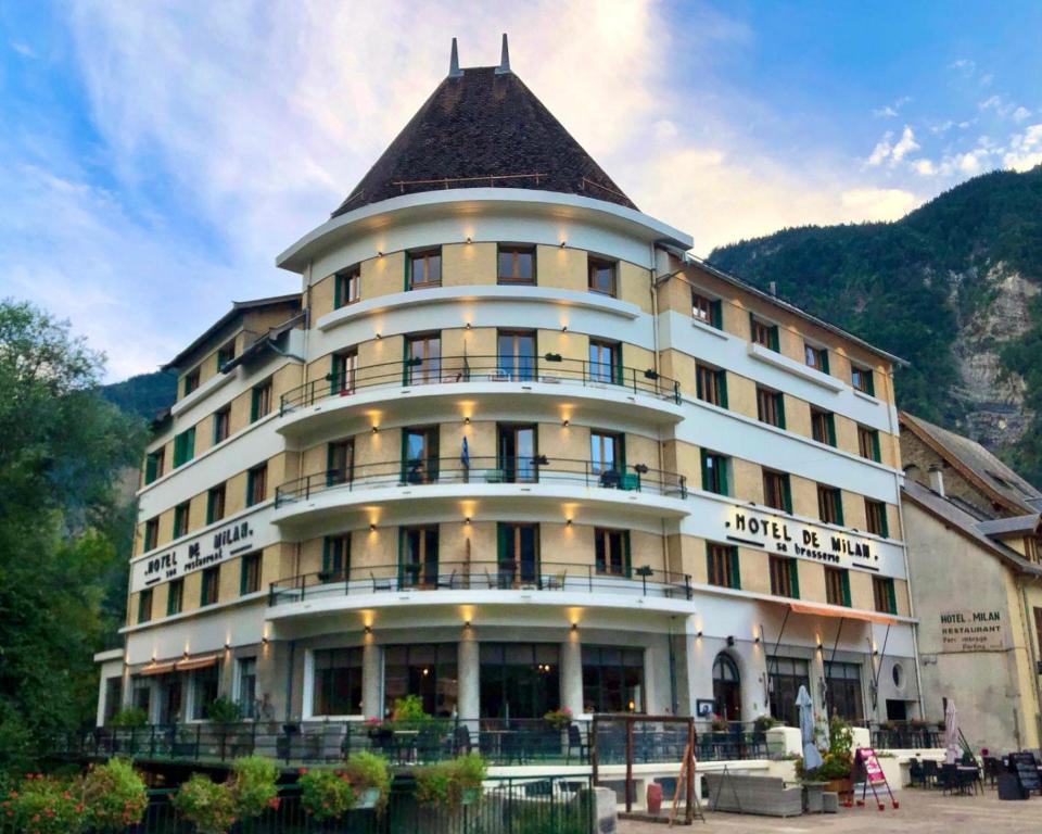 Hotel de Milan Sa Brasserie with arched windows, covered terrace and outdoor seating at the foot of a mountain at Sport'Hotel-Aparthotel de Milan in Le Bourg-dʼOisans