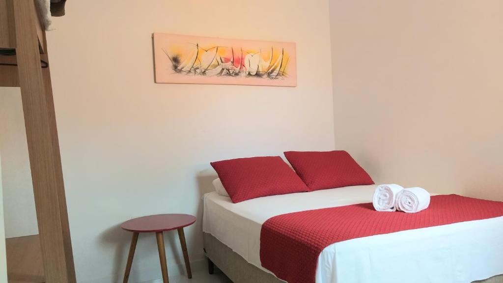 een slaapkamer met een bed met rode kussens en een kruk bij Flor de Peroba Flats #3 Vermelho - Maragogi - AL in Maragogi