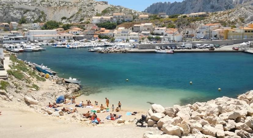 Un groupe de gens sur une plage près d'un port dans l'établissement Au cœur du Parc National du Massif des Calanques, la Flibuste des Goudes, Maison 2 chambres, climatisée, jardins, solarium, proche plage, large vue mer, à Marseille