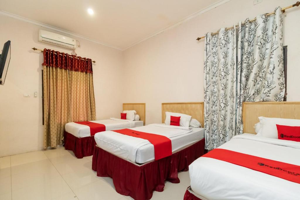 three beds in a room with red and white at RedDoorz At Fella Homestay Medan in Medan