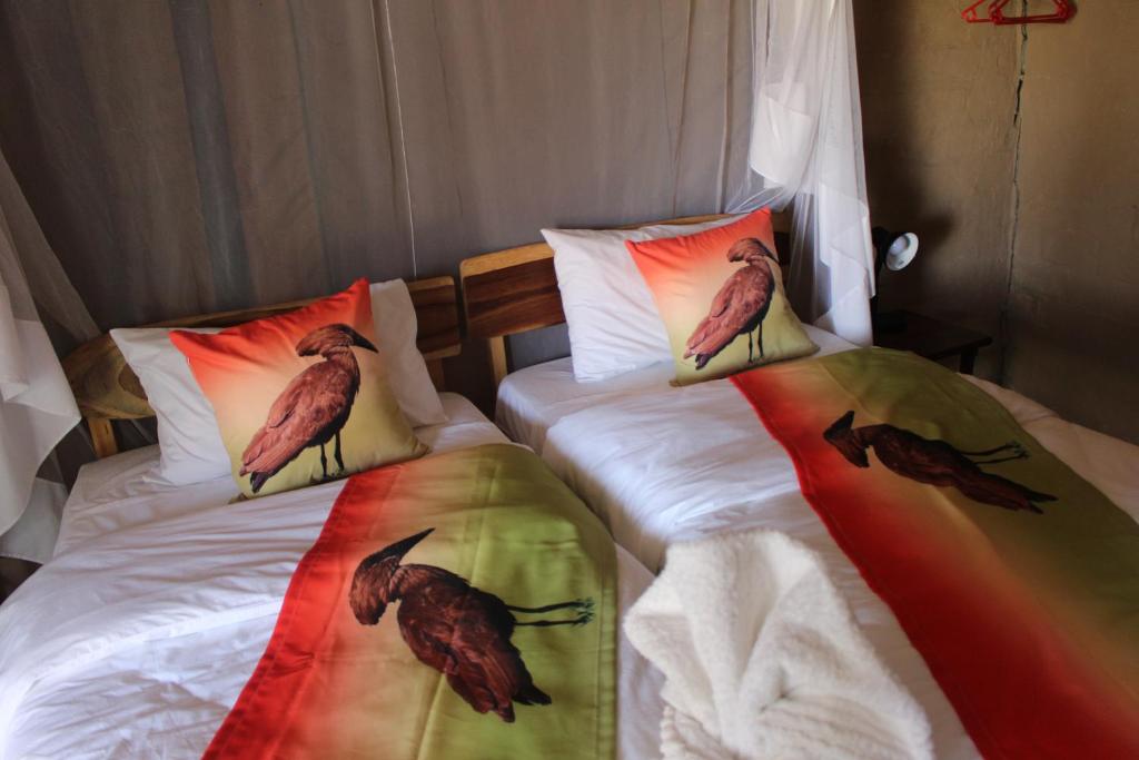 2 Betten mit Vögeln auf den Kissen in einem Schlafzimmer in der Unterkunft Mukolo Cabins & Camping in Kongola