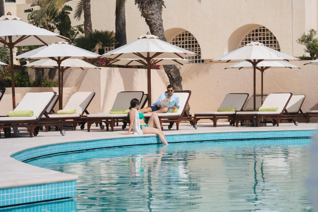 a man and a young girl sitting on the edge of a swimming pool at The Residence Tunis in Gammarth
