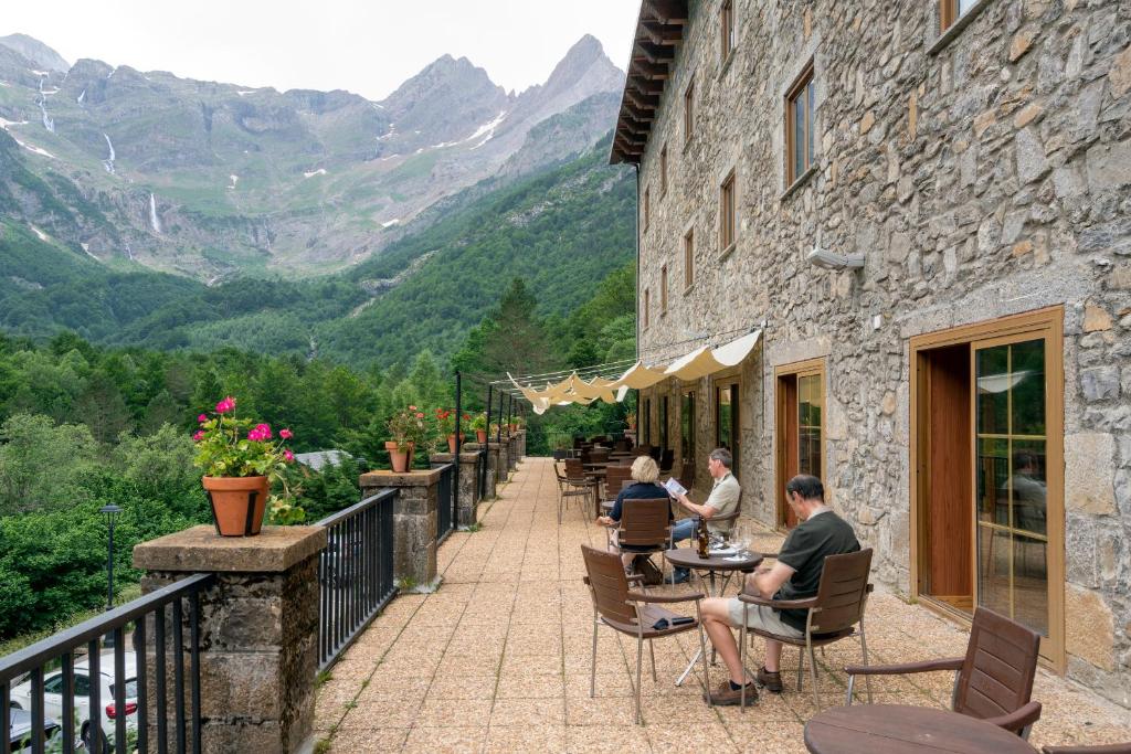 un grupo de personas sentadas en mesas en un balcón con montañas en Parador de Bielsa, en Espierba
