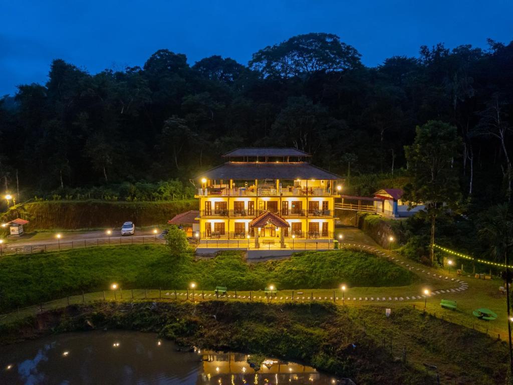 a large building at night with a pond at The Hosteller Coorg Rainforest, Madikeri in Madikeri
