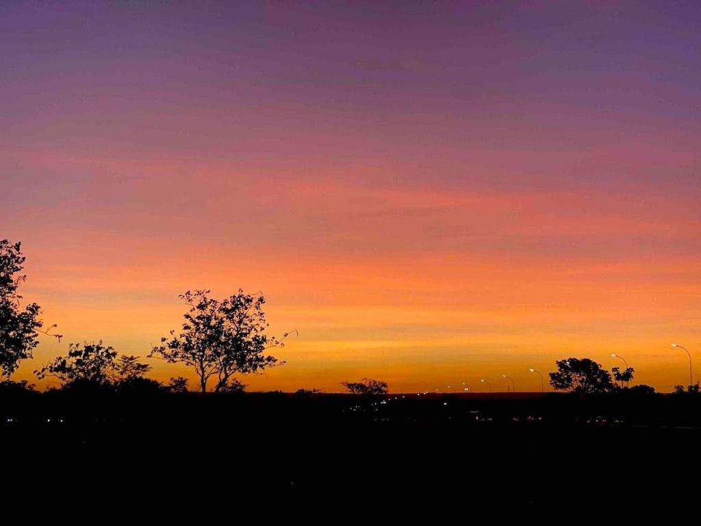 a sunset over a field with trees in the foreground at Brisas do Lago - Apartamento 7 in Brasilia
