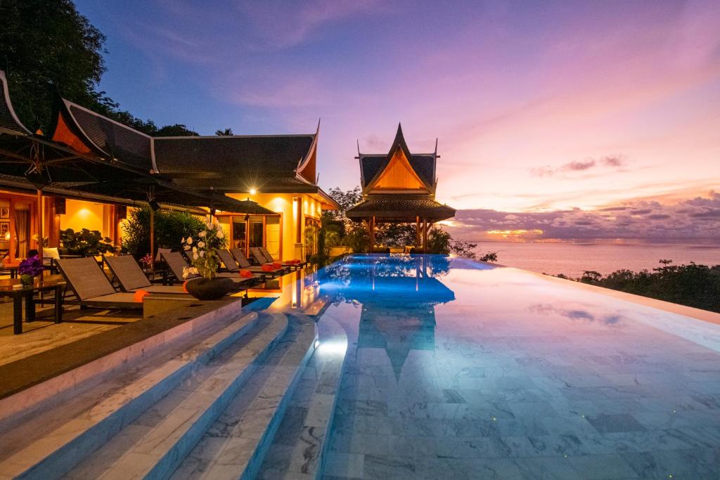 a pool at a resort with a sunset in the background at Baan Phu Prana Boutique Villa in Surin Beach