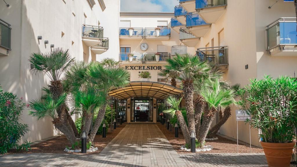 a hallway with palm trees in front of a building at Hotel Excelsior in Lido di Jesolo