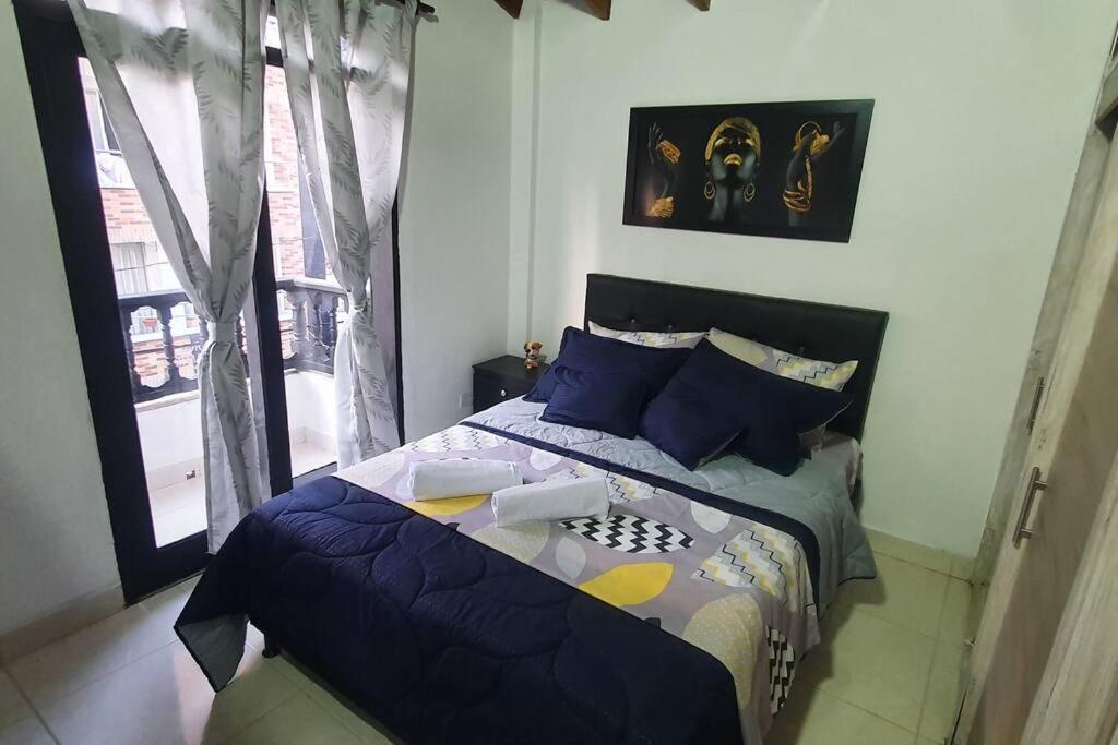 a bedroom with a bed with blue pillows and a window at central apartamento al lado del polideportivo sur de envigado in Envigado
