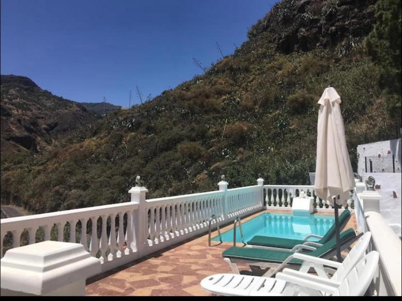 a patio with a pool and a umbrella and chairs at Casa Rural La Yedra San Mateo in Arbejales