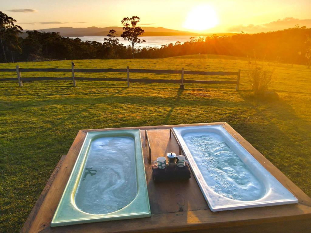 a hot tub in a field with the sunset in the background at Farm Stay & Iconic Water Views - 32 Zachary Drive in Mallacoota