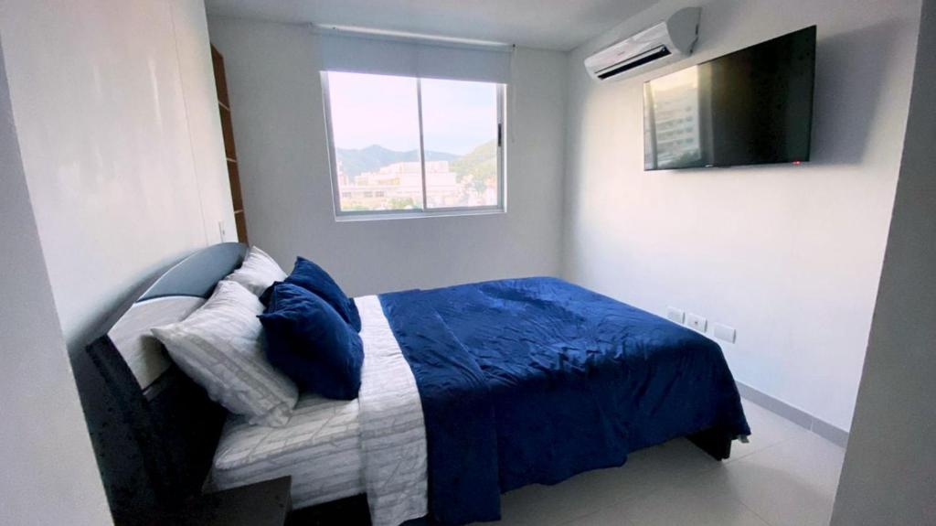 a bedroom with a bed with a blue blanket and a television at apartamentos-rodadero in Gaira