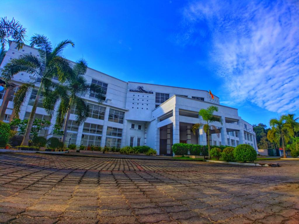 a large white building with palm trees in front of it at Kolonne RIverside Garden Hotel in Avissawella