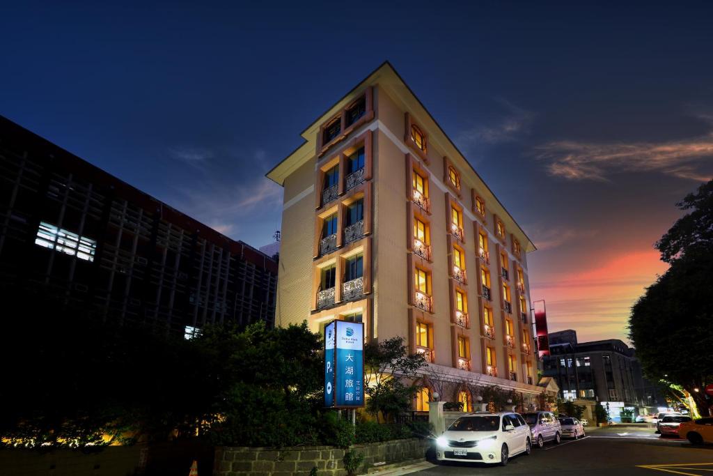 een witte auto geparkeerd voor een hoog gebouw bij Archess Hotel in Taipei