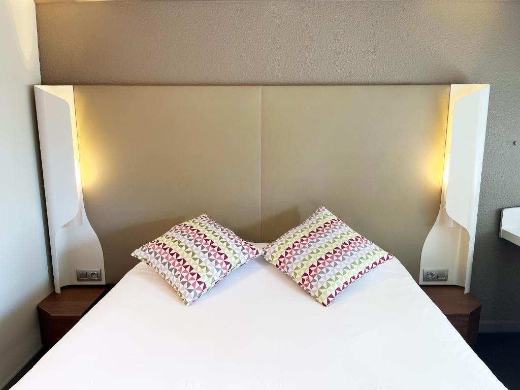 Duas almofadas em cima de uma cama branca em Campanile Epinay sur Orge Savigny Sur Orge em Épinay-sur-Orge