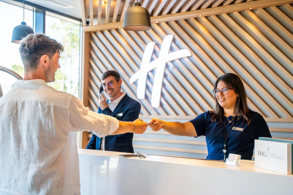 Un uomo e una donna che stringono la mano a un bancone di Holiday Inn - Bordeaux-Merignac, an IHG Hotel a Mérignac