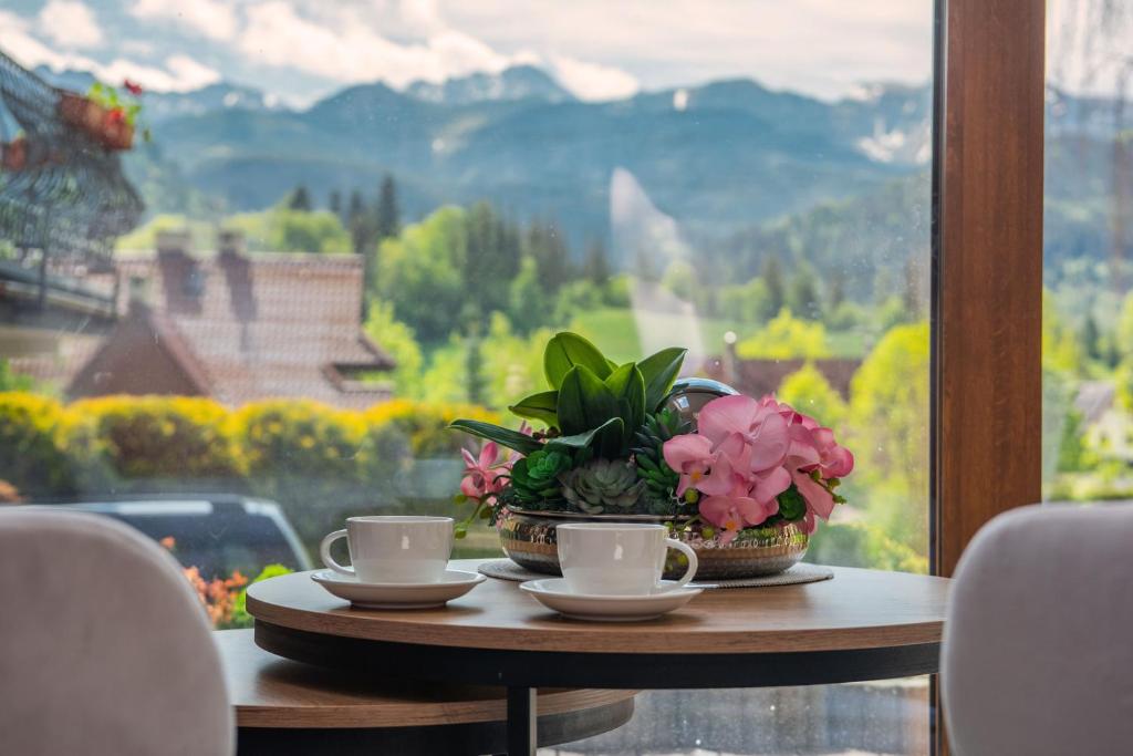 un tavolo con tazze e fiori su un tavolo con finestra di Willa Alesandro a Zakopane