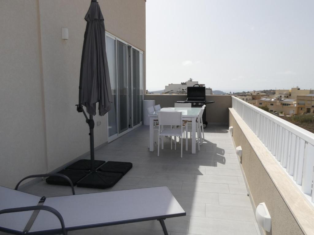 uma varanda com um guarda-sol, mesas e cadeiras em Blue Sky Apartments em Mġarr