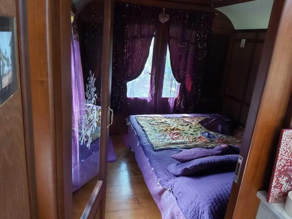 - une chambre avec un lit doté de draps violets et une fenêtre dans l'établissement La roulotte d'alany, à Grayan-et-lʼHôpital