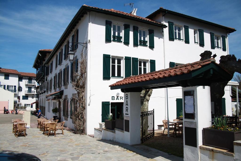 un bâtiment blanc avec volets verts dans une rue dans l'établissement Hôtel de la Rhune, à Ascain