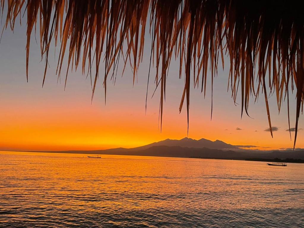 een zonsondergang over het water met bergen op de achtergrond bij Star Bar and Bungalows in Gili Air