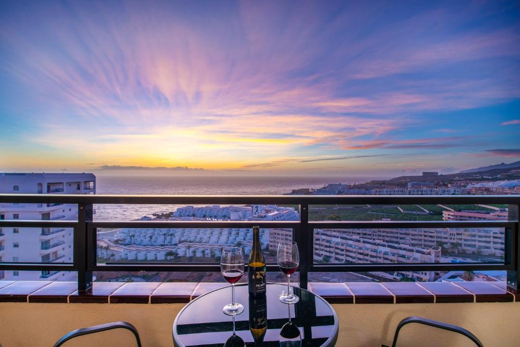 uma mesa com copos de vinho numa varanda com um pôr-do-sol em Ocean View Experience em Adeje