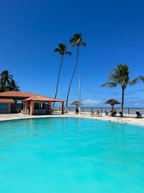 a swimming pool next to a beach with palm trees at MARAGOGI FLAT BEIRA MAR in Maragogi