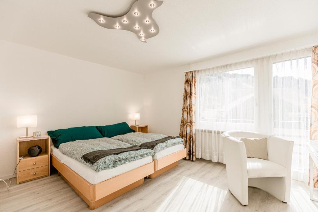 a white bedroom with a bed and a chair at Ferienwohnung Ägerisee in Oberägeri