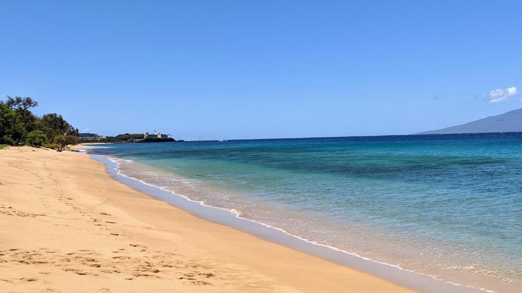 uma praia arenosa com o oceano e montanhas ao fundo em Honua Kai - Hokulani 414 em Lahaina