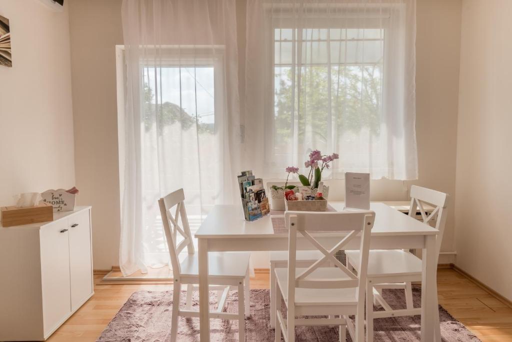 a white dining room table with white chairs and a window at Lianne Apartman in Miskolctapolca