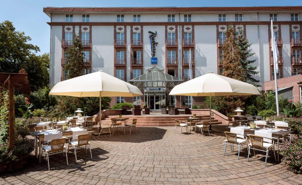 eine Terrasse mit Tischen und Sonnenschirmen vor einem Gebäude in der Unterkunft Radisson Blu Hotel Halle-Merseburg in Merseburg