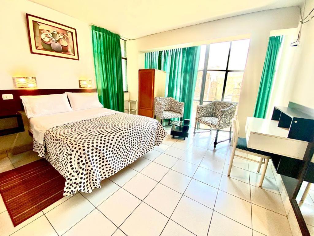1 dormitorio con 1 cama con cortinas verdes y escritorio en CasaHotel Jockey Plaza Mall en Lima