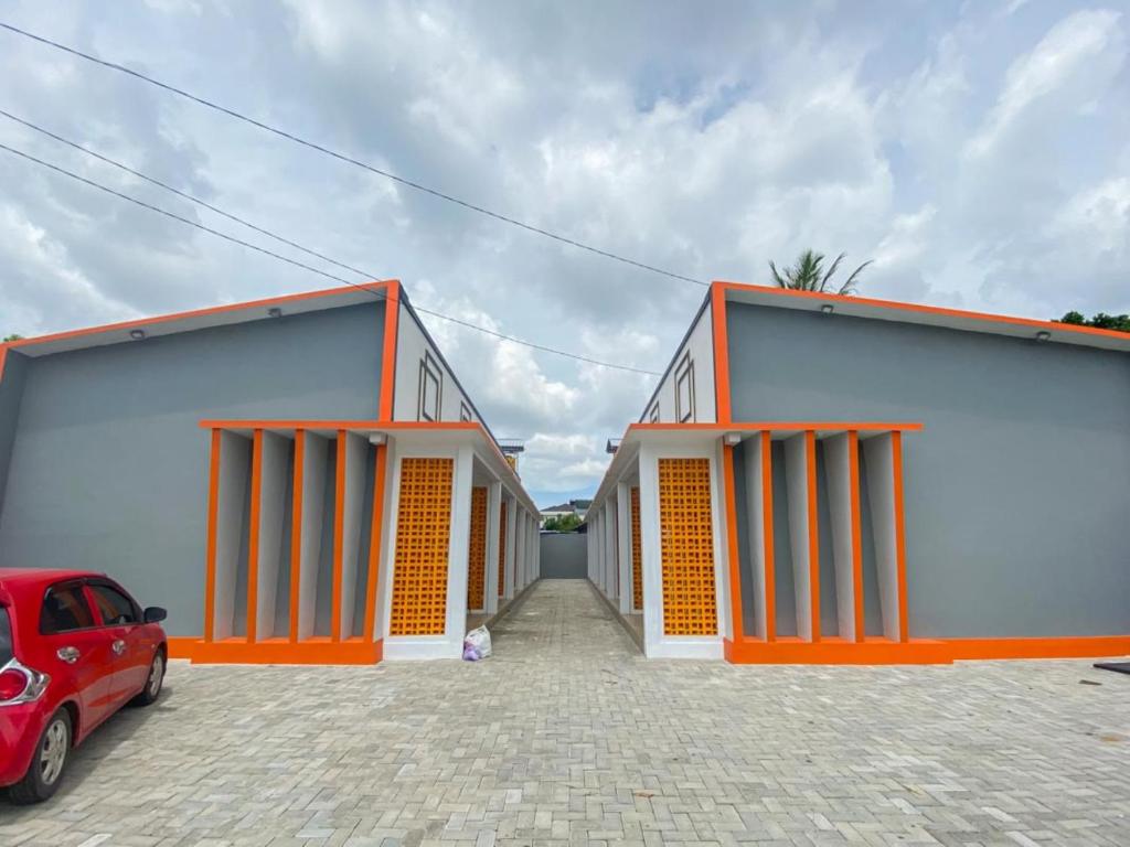 zwei Gebäude mit orangefarbenen Türen und einem davor geparkten roten Auto in der Unterkunft RedDoorz Plus at Orange Diponogoro Palangkaraya in Palangkaraya