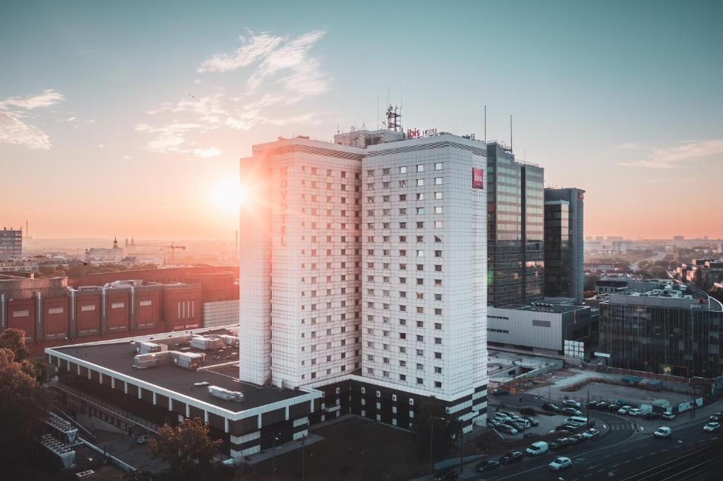 een hoog wit gebouw met de zonsondergang erachter bij Ibis Poznan Centrum in Poznań