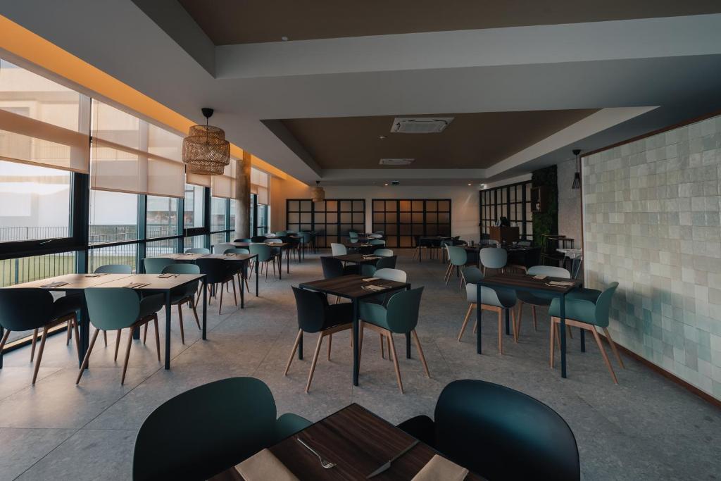 a restaurant with tables and chairs and windows at Porto Covo Praia Hotel & SPA in Porto Covo