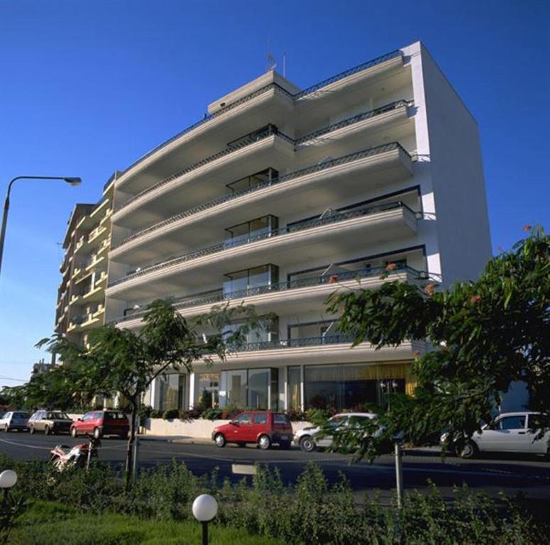 un grand bâtiment blanc avec des voitures garées devant lui dans l'établissement Hotel Elena, à Xánthi