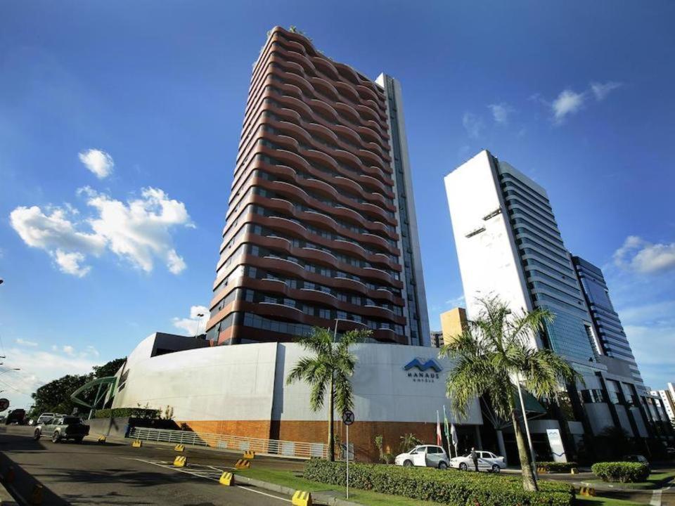 a tall building next to a building with palm trees at Millenium Hotel Flat in Manaus