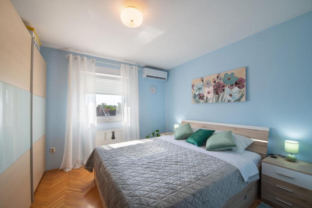 sypialnia z łóżkiem z niebieskimi ścianami i oknem w obiekcie Apartman Silvija w mieście Osijek