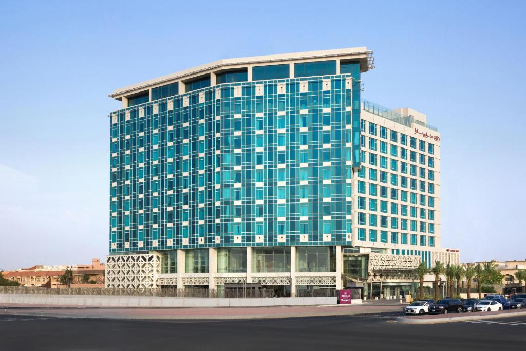 un grand bâtiment en verre avec des voitures garées devant lui dans l'établissement Crowne Plaza - Jeddah Al Salam, an IHG Hotel, à Djeddah