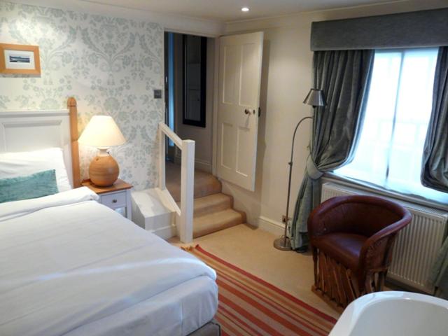 a bedroom with a bed and a chair and a staircase at Manor Green Cottage in Windsor
