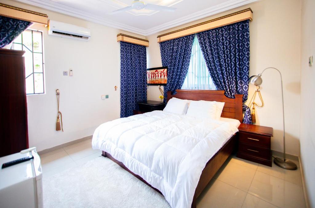 a bedroom with a large bed and blue curtains at Aduk Guest House Airport City Accra in Otele