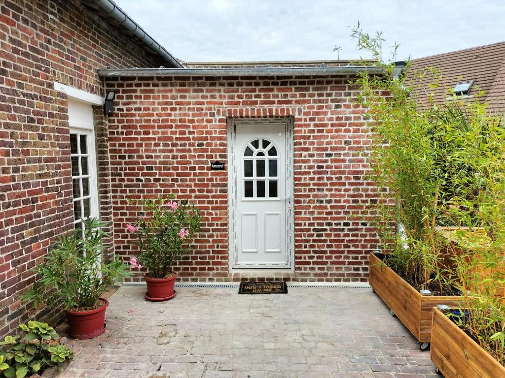ein Backsteingebäude mit einer weißen Tür und einigen Pflanzen in der Unterkunft Studio - Au fond de la cour in Lacroix-Saint-Ouen